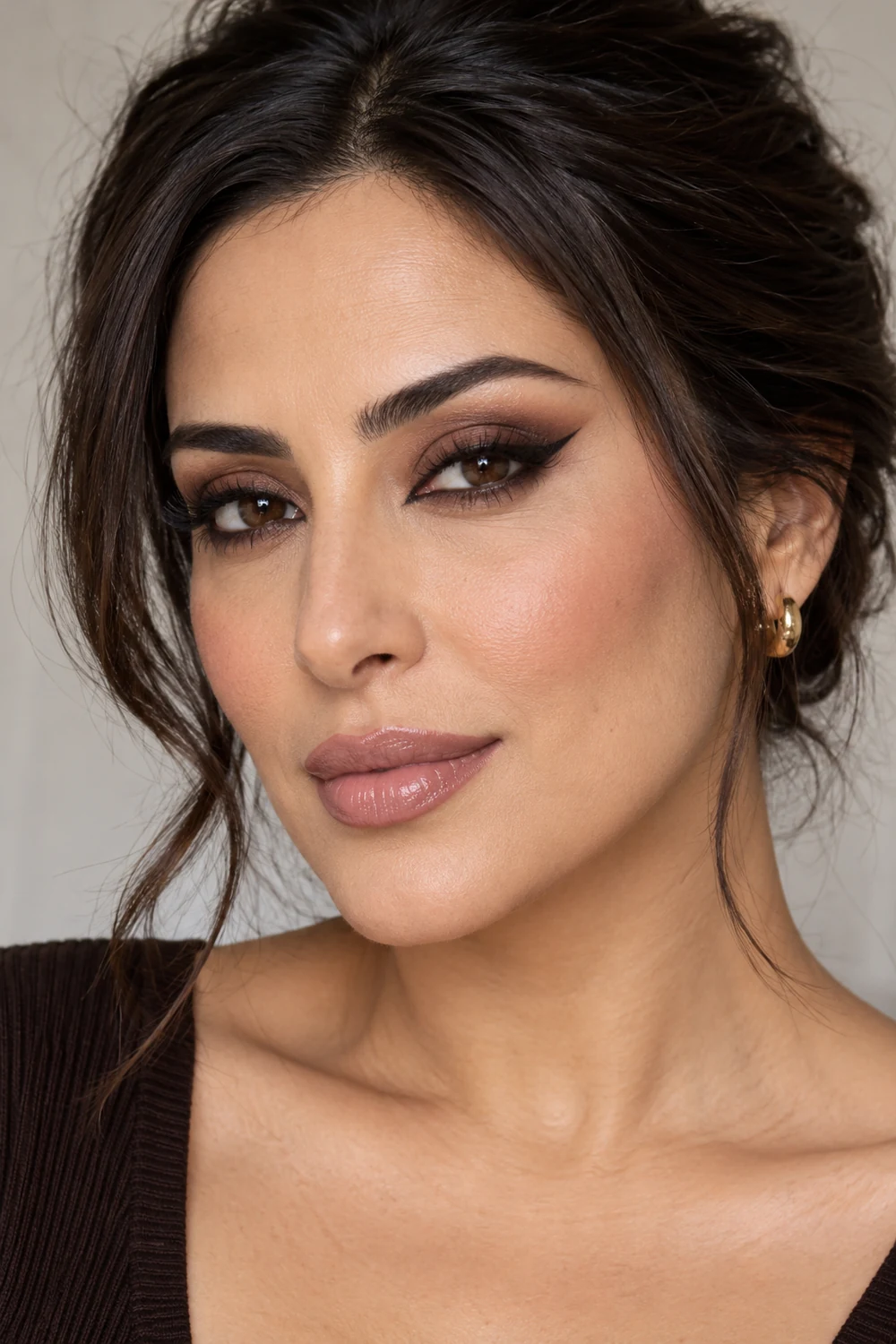 Close beauty portrait of an adult woman with elongated espresso brown smokey eyes, a sharp pointed black-brown liner flick, beige-rose blush, and pale mauve gloss.