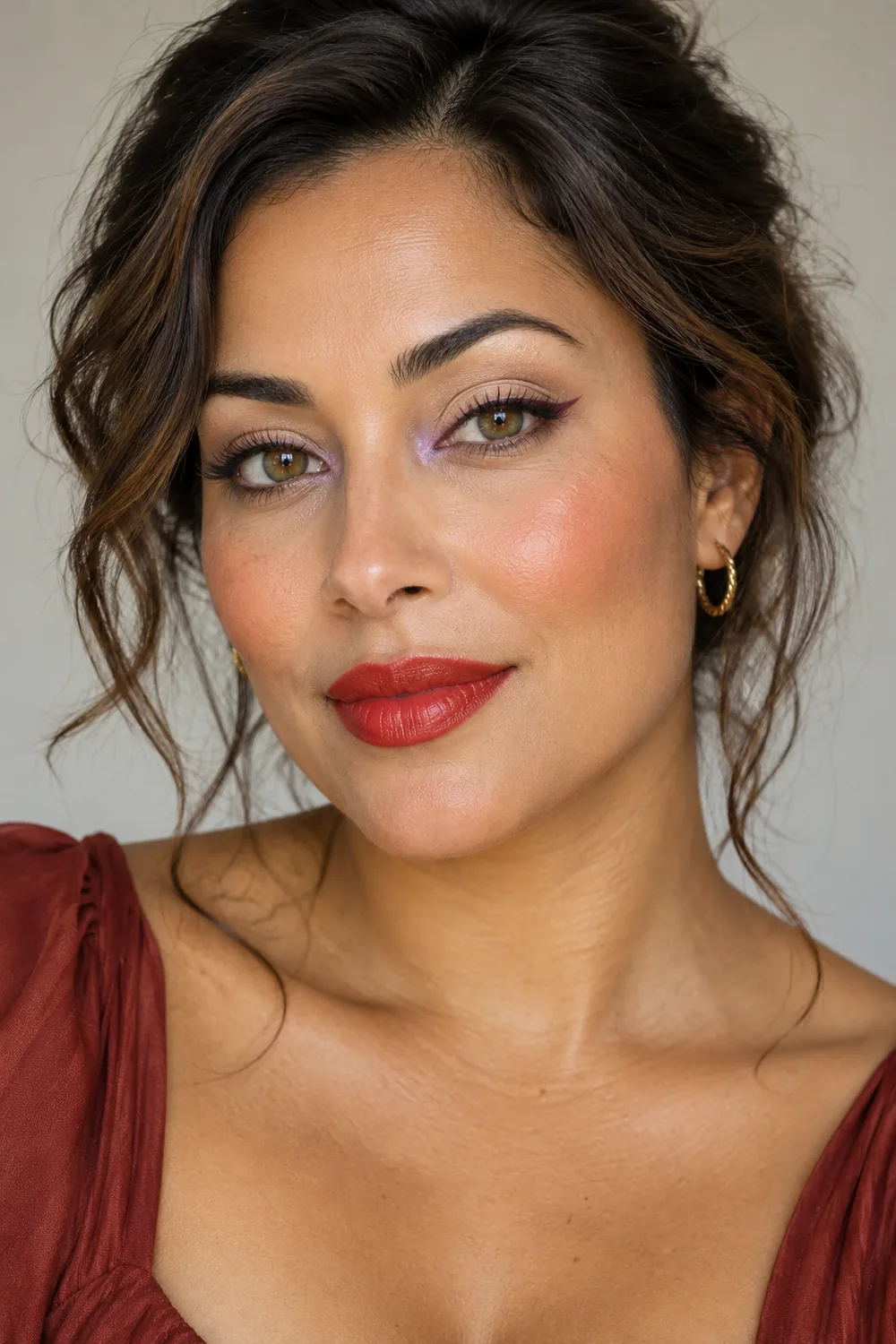 Adult woman with warm tomato-red satin lipstick, lavender inner-corner shadow, plum flicked liner, and apricot blush.
