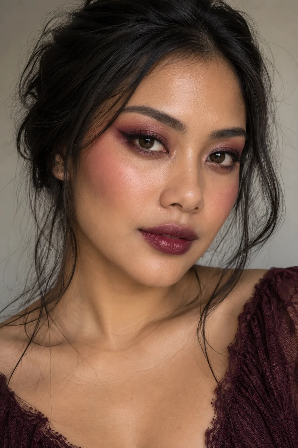 Close-up portrait of an adult woman with rose-burgundy shadow, softly extended blush, tiny black outer-corner flicks, and wine-colored lips.