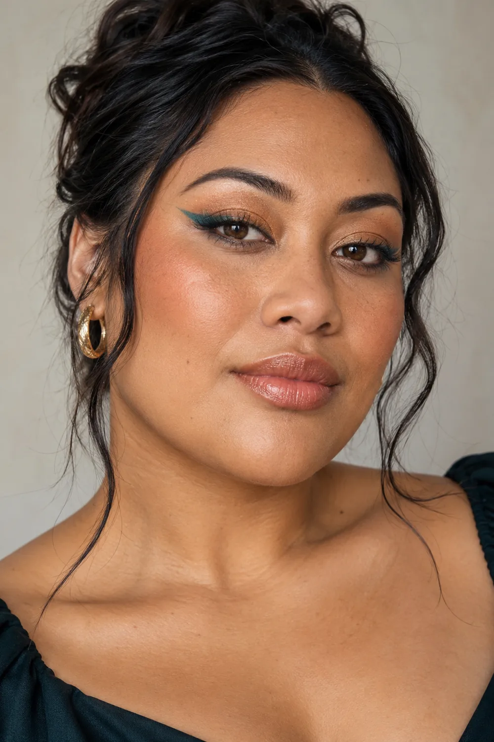 Adult woman with bronze eyeshadow, deep teal winged liner, apricot blush, and nude satin lipstick, photographed against a neutral background.