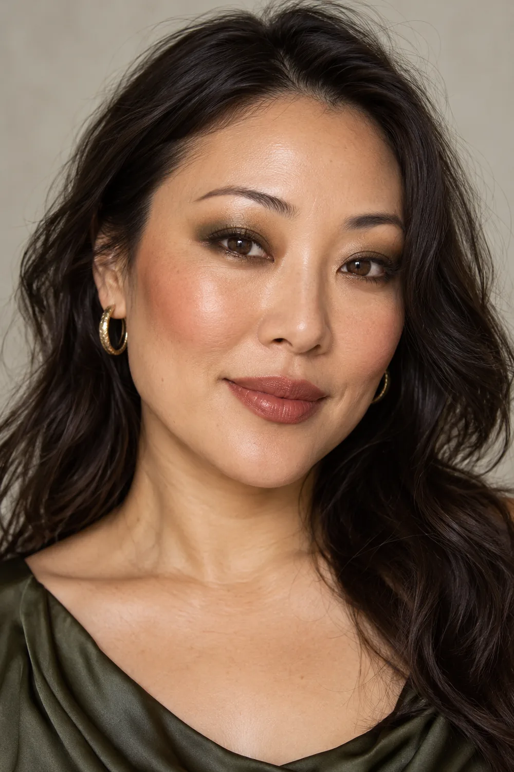 Close portrait of a fictional East Asian adult woman wearing olive eye shadow, bronze liner, terracotta blush, and cinnamon-rose satin lipstick.