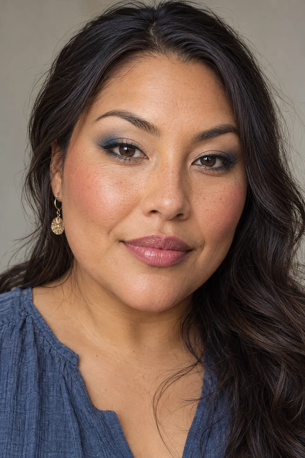 Fictional adult woman with open hooded brown eyes, beige shadow, slate-blue outer eye accents, charcoal liner, mauve blush, and pink-beige satin lips.