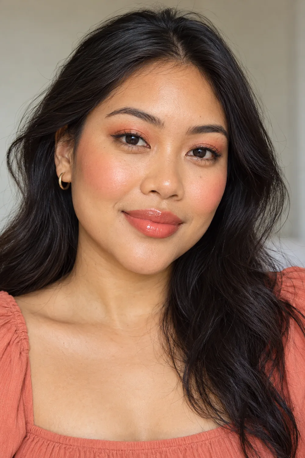 Fictional adult woman with open hooded dark brown eyes wearing soft coral lid shadow, close brown liner, pink-coral blush, and sheer coral lip color.