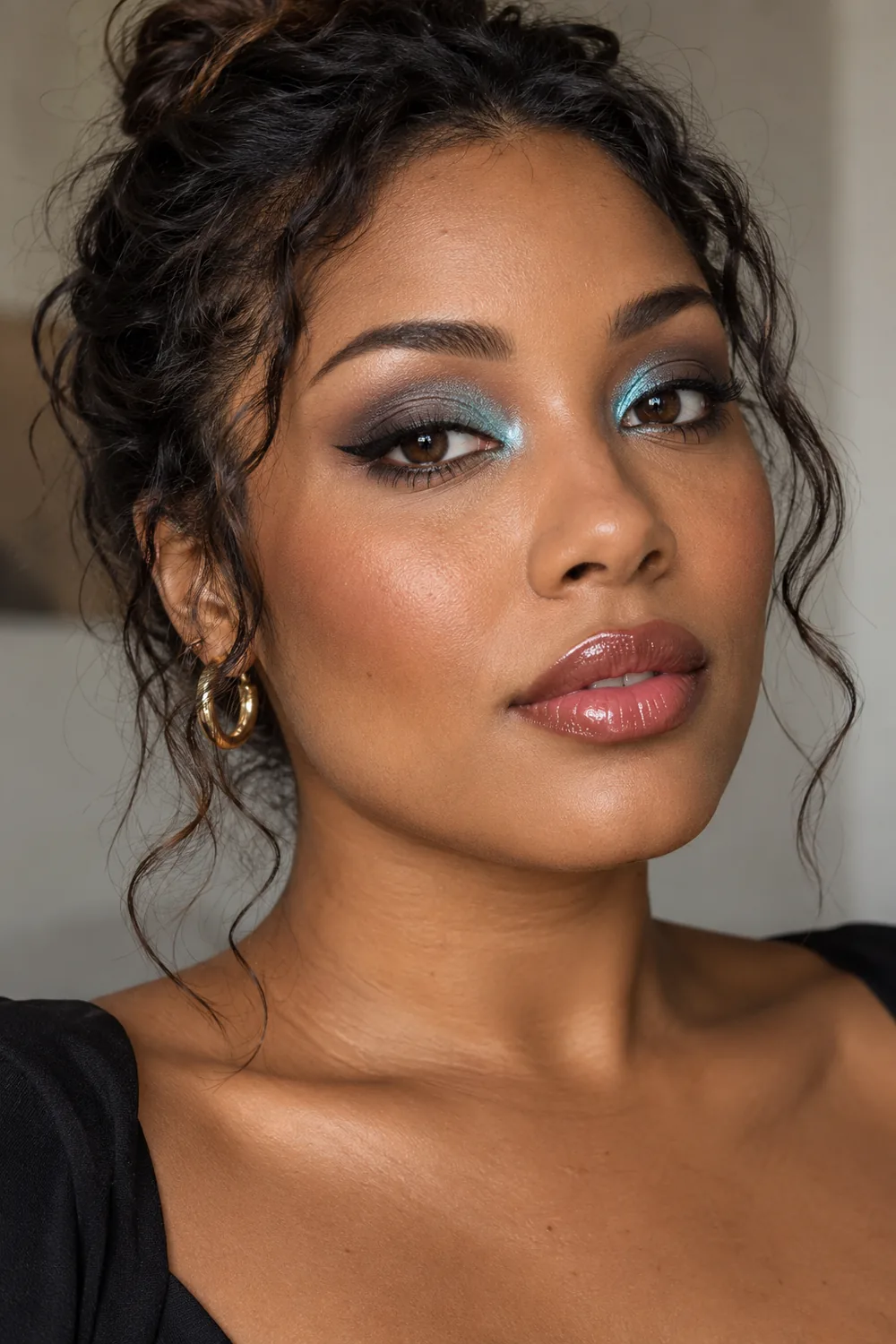 Adult woman with medium-deep skin and brown eyes wearing teal inner-lid shimmer, slate shadow, extended black wing, cinnamon blush, and rose gloss.