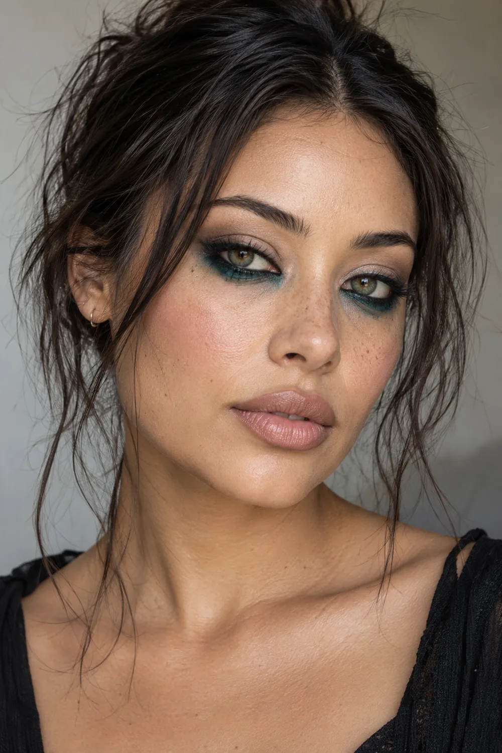 Adult woman with green eyes, deep teal shadow smudged beneath the lower lashes, soft black upper liner, pale sand lids, cool pink blush, and nude satin lips.