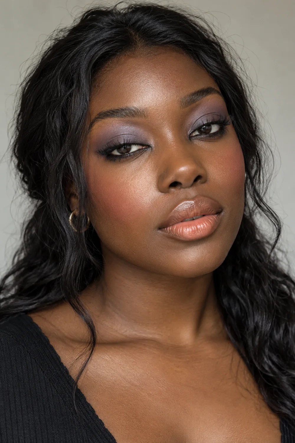 Adult woman with lavender crease shadow, smoky grey lash line, softly blurred short liner, peach blush, and satin peach lips.