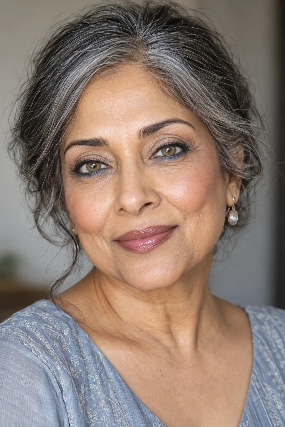 Fictional mature South Asian woman with green-brown hazel eyes, ivory-beige lids, slate-blue lower lash shadow, subtle navy tightline, beige-rose blush, and mauve lips.