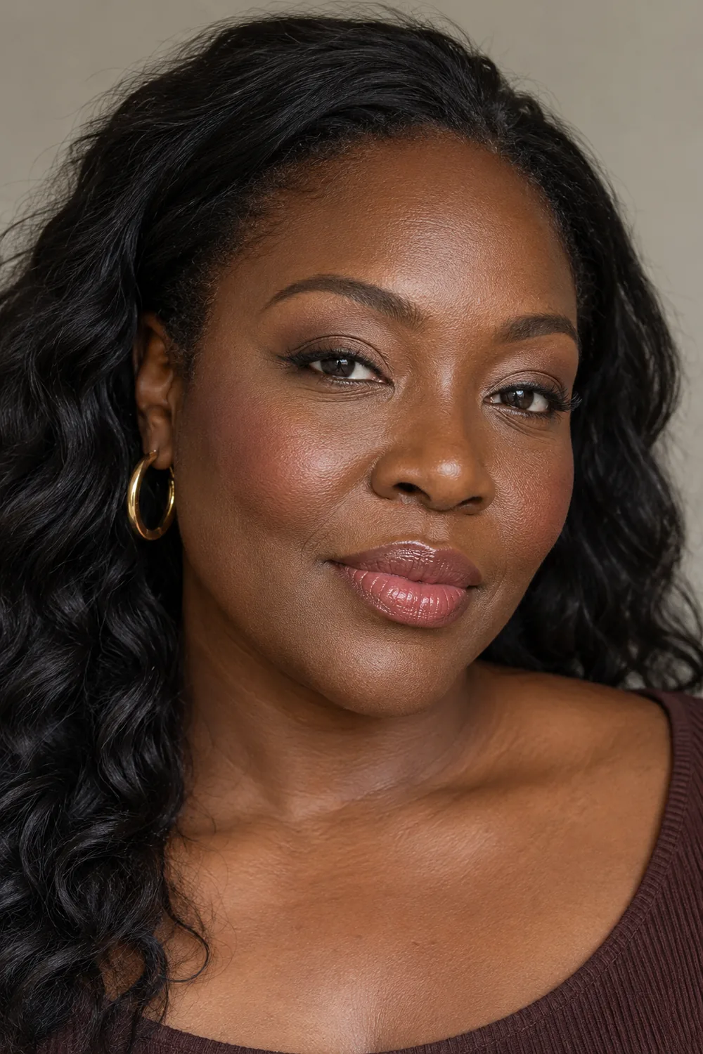 Adult woman with very deep brown skin, softly shaded taupe creases, subtle brown liner, rosewood blush, and muted rose gloss.