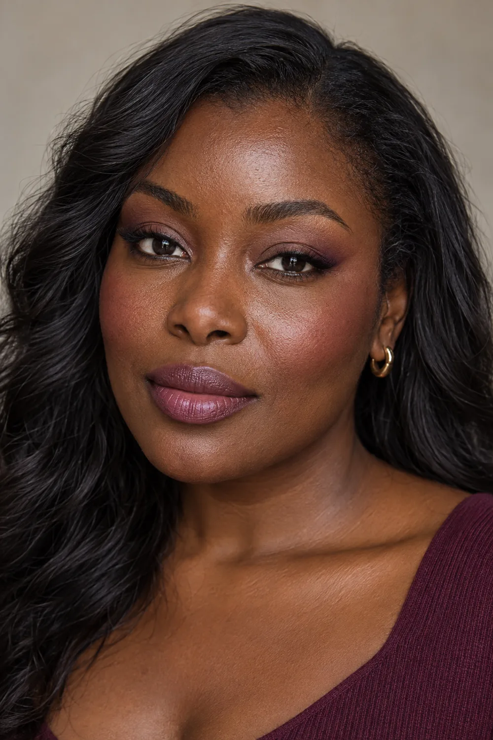 Beauty-editorial portrait of a woman with deep mahogany skin, soft plum outer-corner shadow, berry-rose blush, and muted mauve satin lipstick.