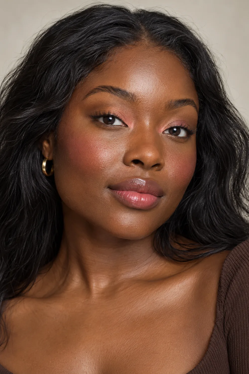 Close vertical portrait of a woman with deep cocoa skin, peach inner-lid shadow, high raspberry blush, and softly glossy raspberry lips.