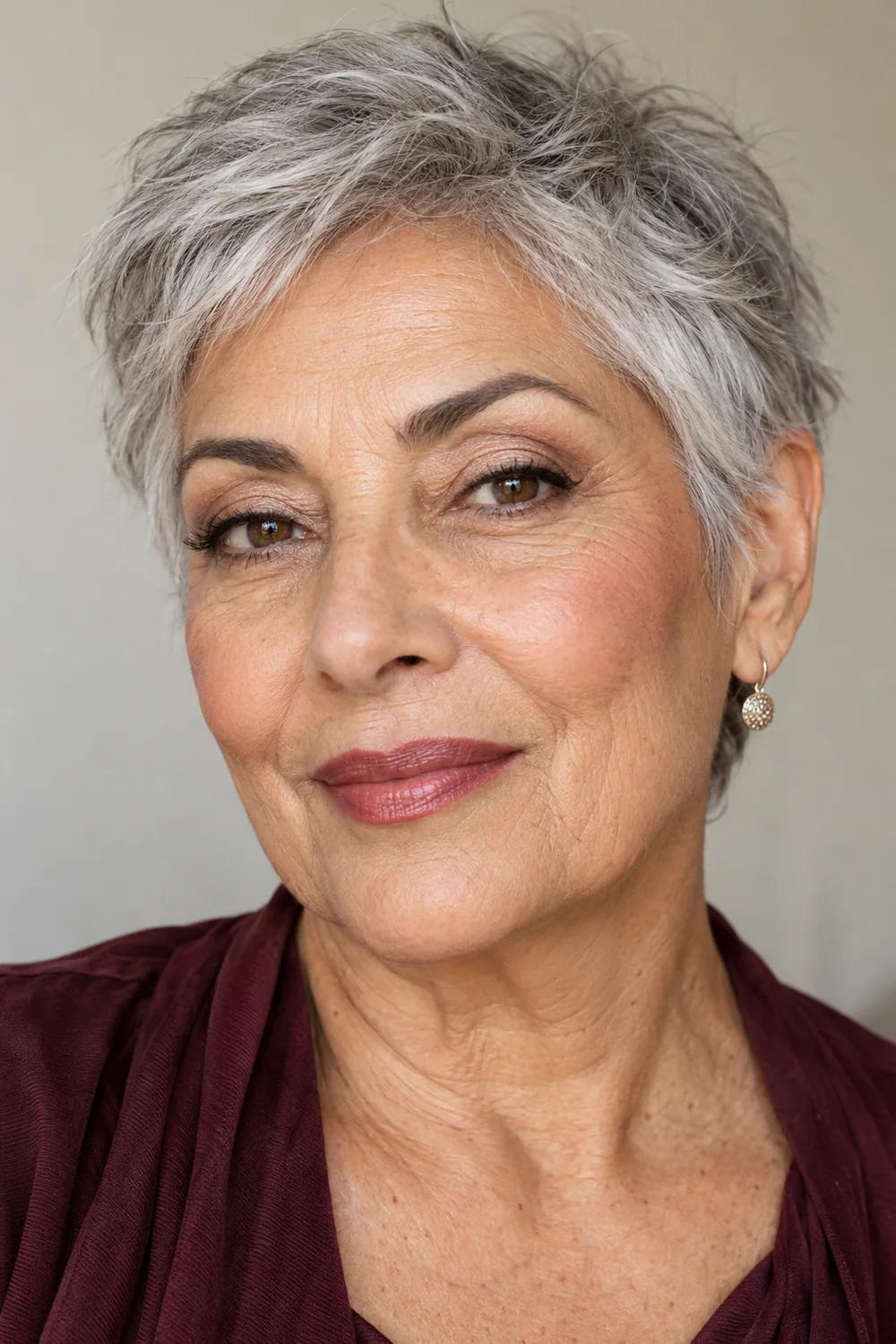 Mature woman with olive skin and silver pixie hair wearing soft brown crease shadow, champagne lid shimmer, close upper lash liner, mauve blush, and deeper rose lipstick.