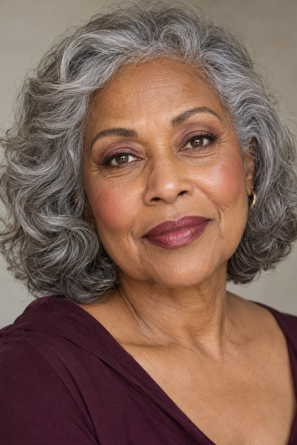 Fictional woman in her late 60s with medium-deep neutral skin, softly blended berry-brown eyeshadow, close brown liner, dusty rose blush, and satin berry lips.