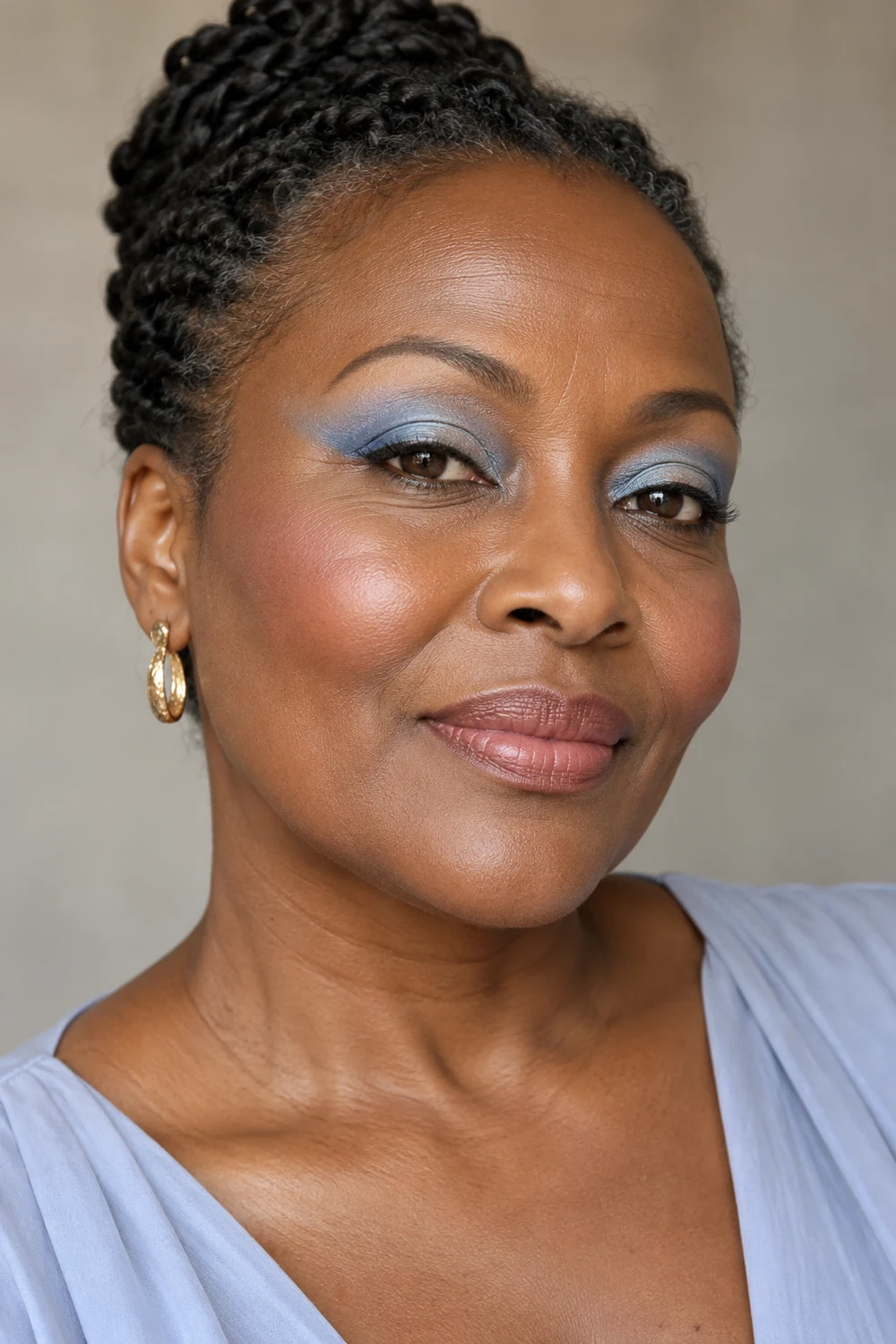 Mature woman with rich dark skin wearing powder-blue eyeshadow swept outward, fine upper-lash liner, dusty rose blush, and nude-rose satin lipstick.