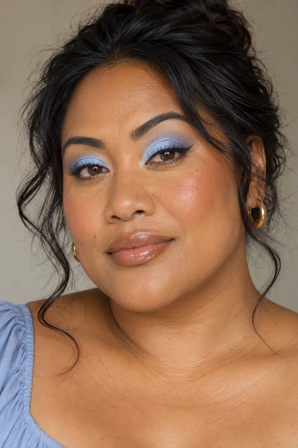 Adult woman with a soft icy-to-cornflower baby-blue lid gradient, short plum-brown liner flick, terracotta blush, and sheer caramel gloss.