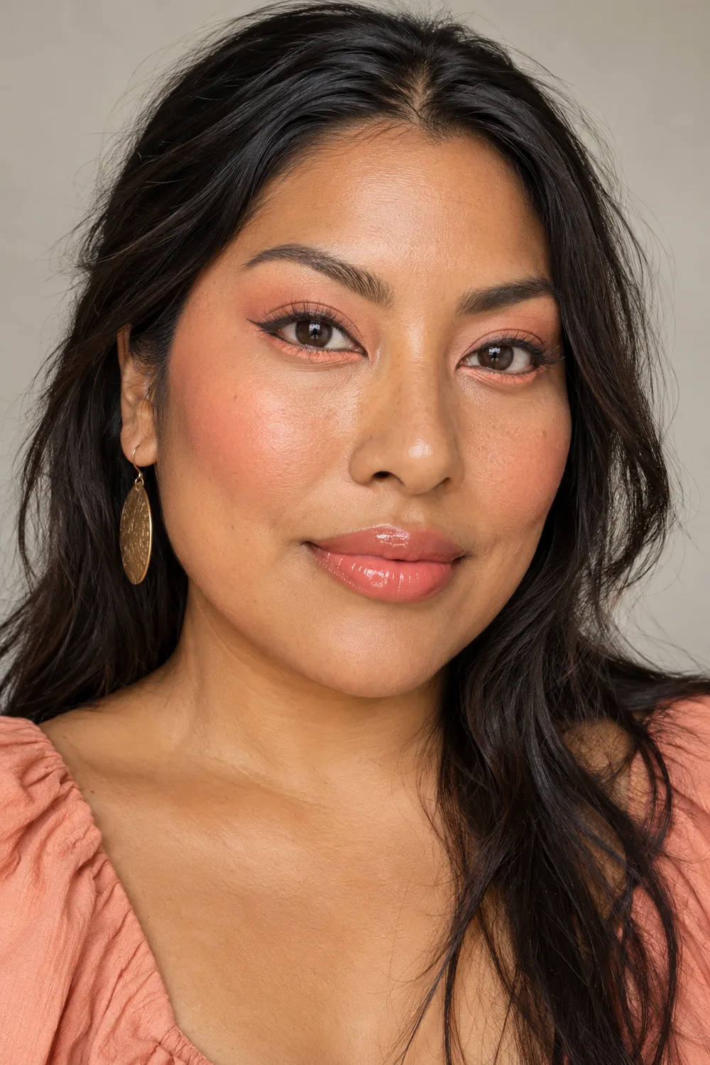 Fictional adult woman with copper skin wearing pale peach eye shadow, a distinct pastel peach lower-lash accent, fine liner, peach blush, and pink-peach gloss.