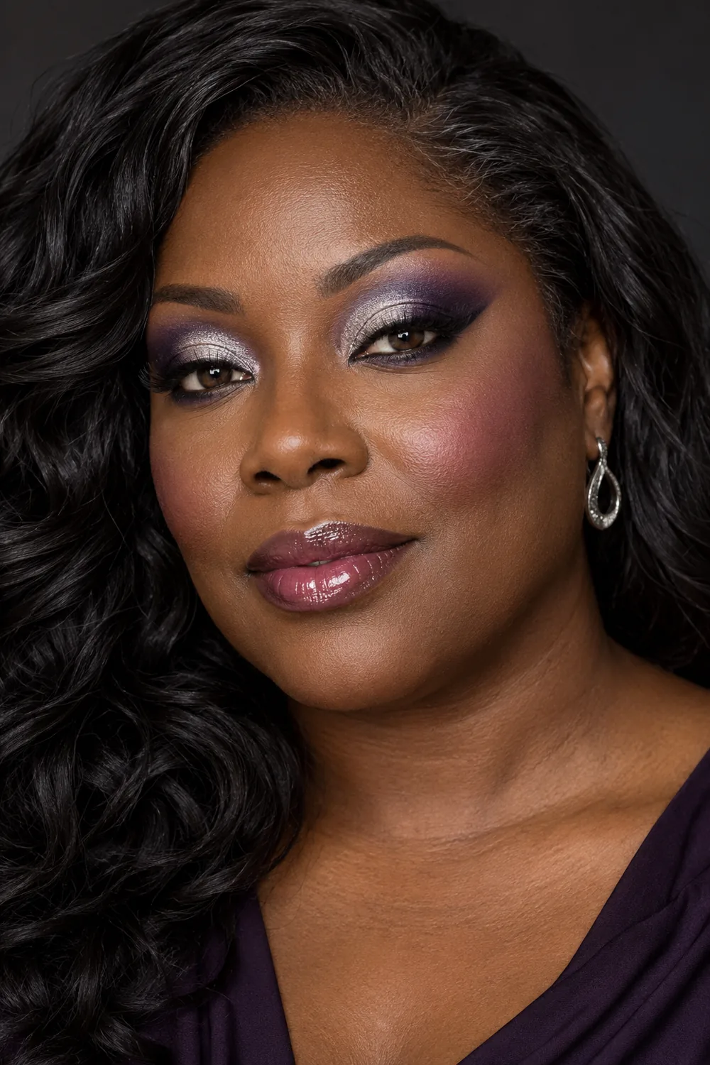 A fictional adult Black woman with deep espresso skin wears smoky violet and reflective silver eyeshadow, charcoal winged liner, plum blush, and glossy berry lips.