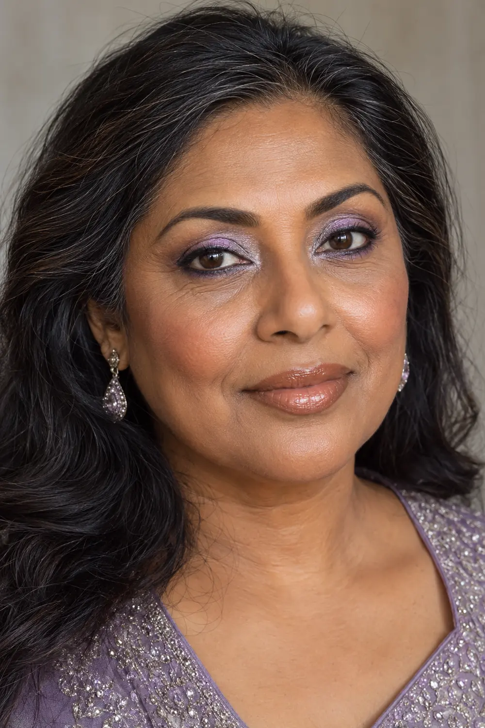 Close vertical portrait of a mature South Asian woman wearing pearly lilac eyeshadow, silver inner-corner highlight, violet lower waterline, cinnamon blush, and caramel nude gloss.