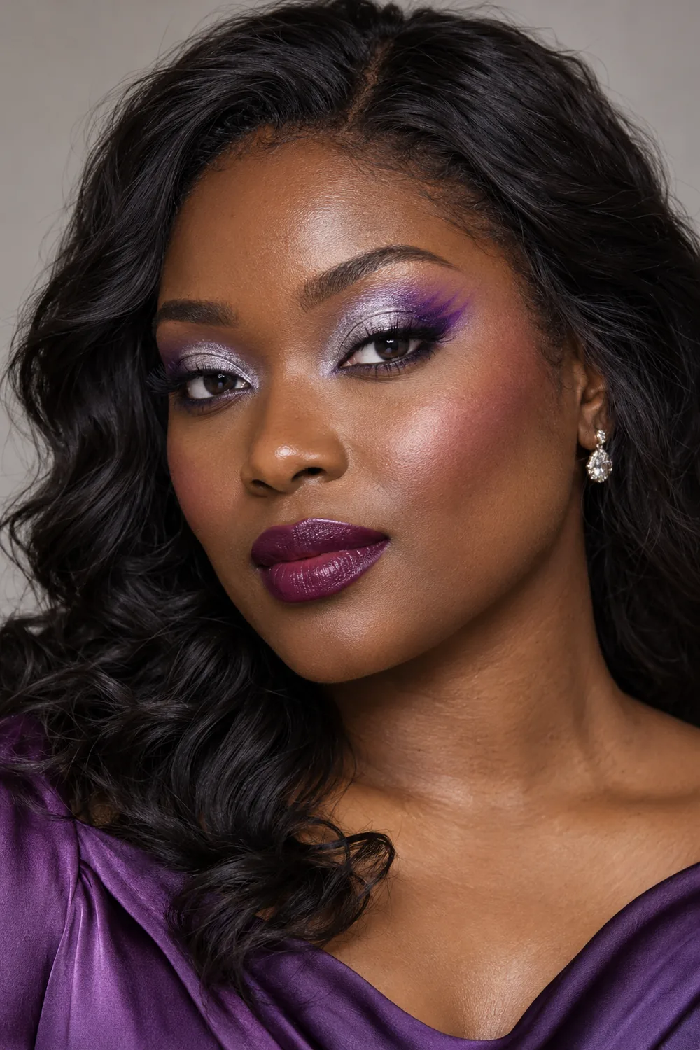 Close-up editorial portrait of an adult Black woman wearing silver shimmer across her lids, pointed violet and lilac outer-corner eyeshadow, rose blush, and deep plum lipstick.