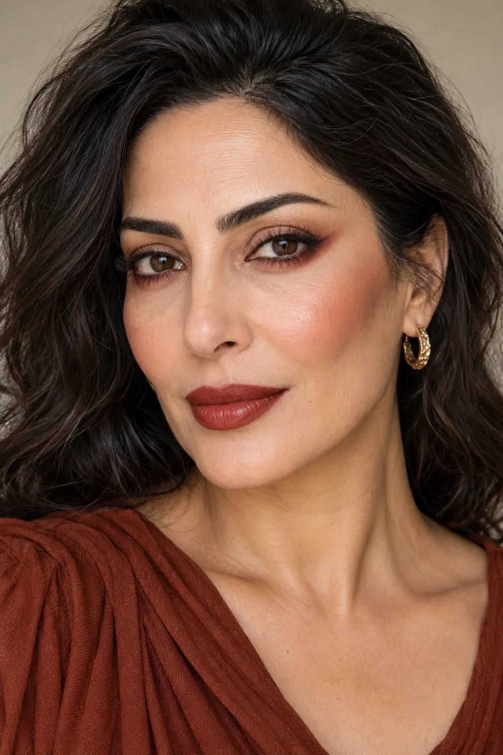 Adult woman with open dark eyes, rust shadow winged outward from the lower lashes, cocoa outer-corner shading, cinnamon blush, and brick-red satin lipstick.