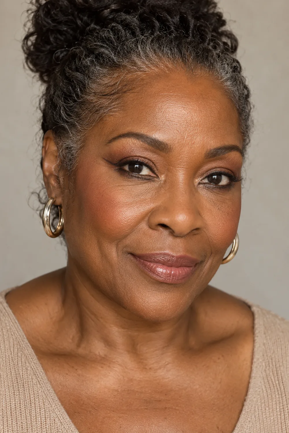Mature Black woman with open dark eyes, soft brown lower-lash wings, champagne inner-corner shimmer, peach blush, and rosy nude balm.