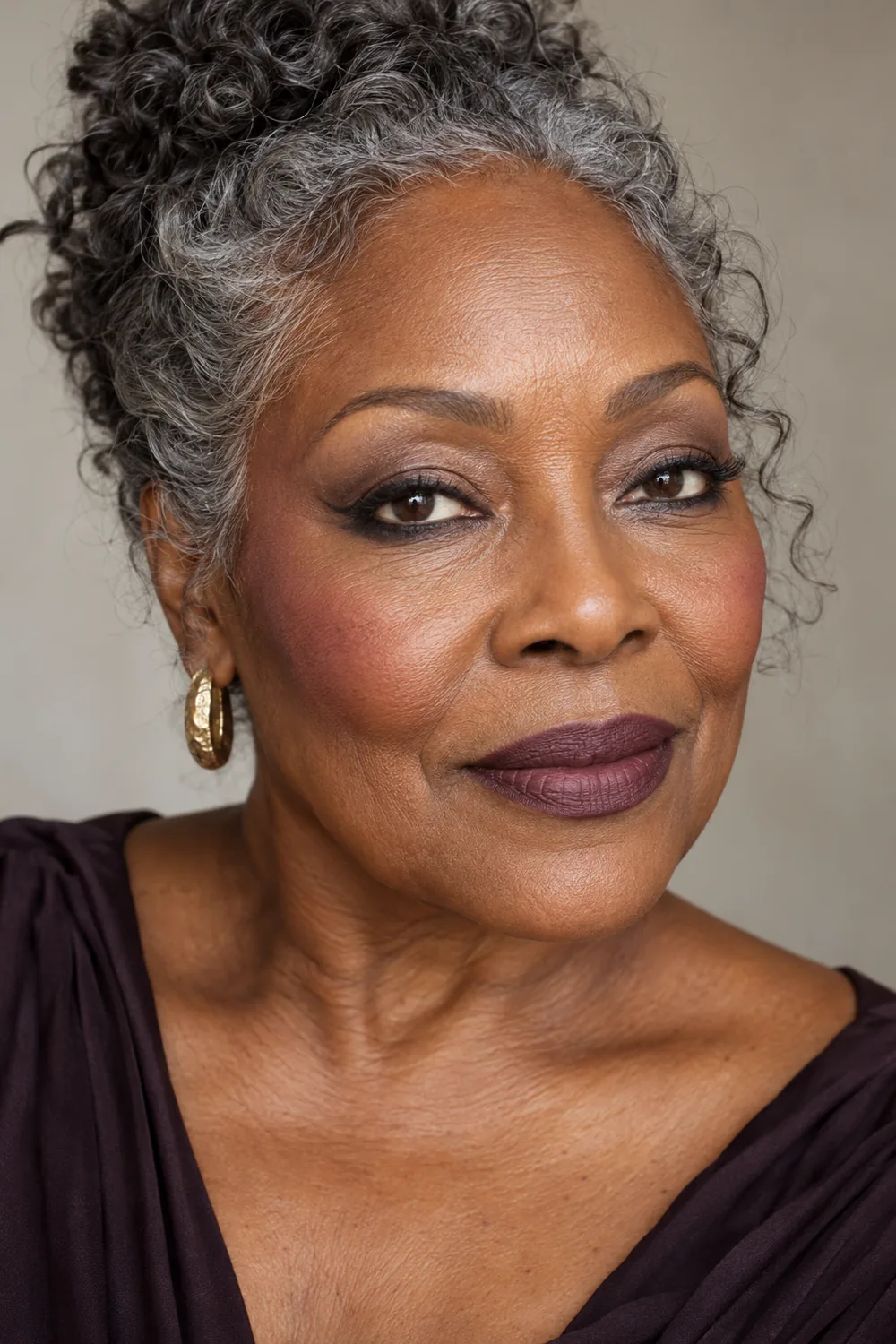 Mature woman with a smoked matte-black lower lash line wing, taupe crease haze, berry blush, and muted plum lipstick.