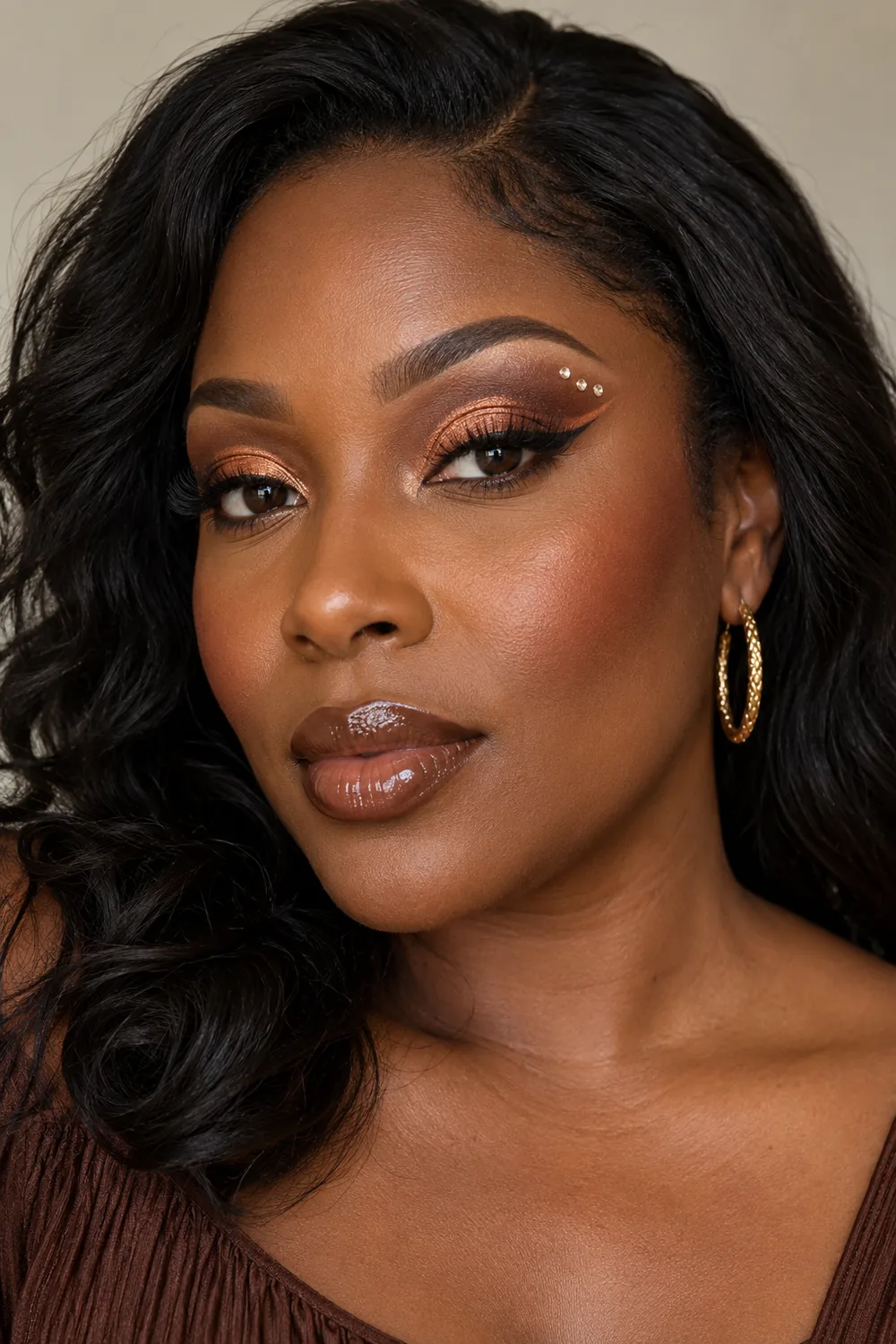 Adult woman with copper foil lid, deep-brown cut crease, bronze tapered wing, three warm-clear gems above the outer crease, cinnamon blush, and cocoa gloss.