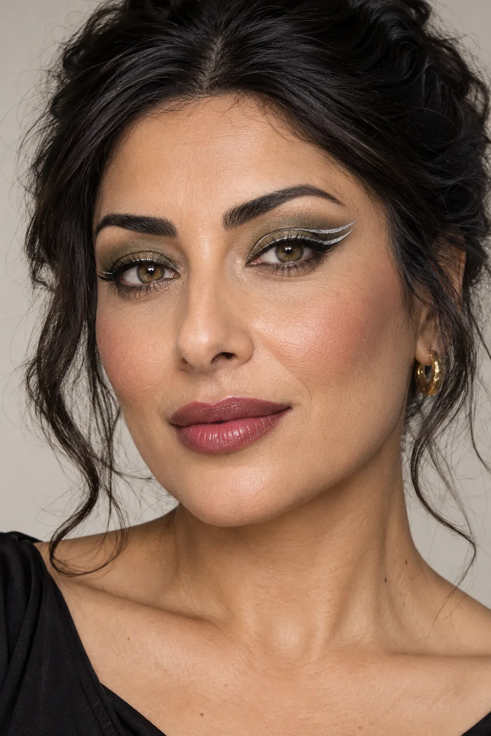 Adult woman with olive shadow, separated double silver eyeliner wings, softly blended cheek color, and berry balm lips.