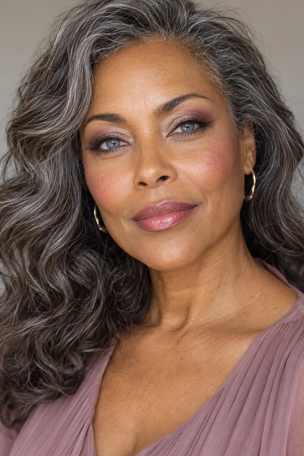 Mature woman with blue eyes, salt-and-pepper hair, taupe and plum eye makeup, mauve blush, and soft rose lipstick.