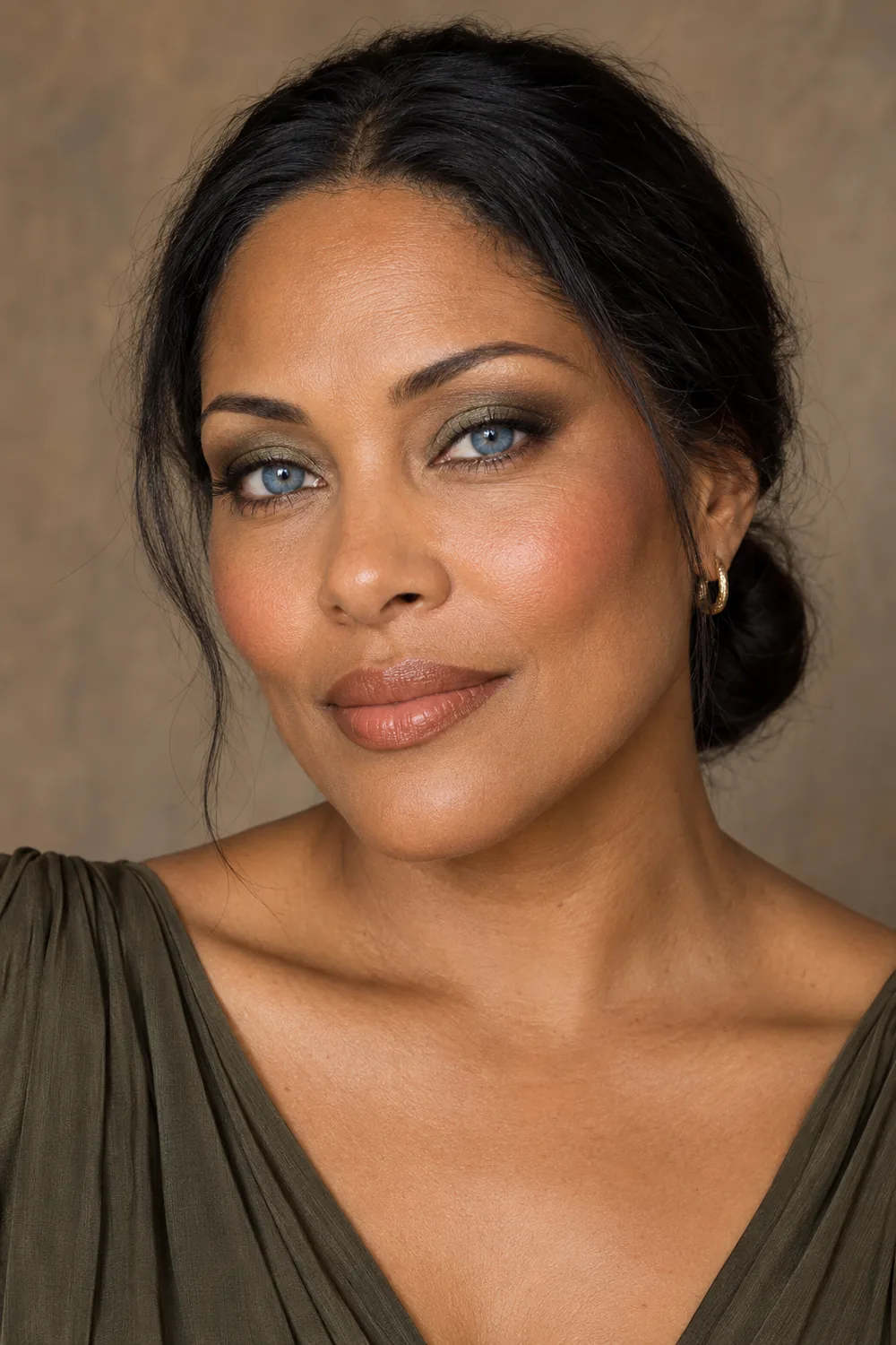 Adult woman with blue eyes wearing olive-bronze lid shadow, softly curved brown liner, apricot blush, and cinnamon nude satin lipstick.