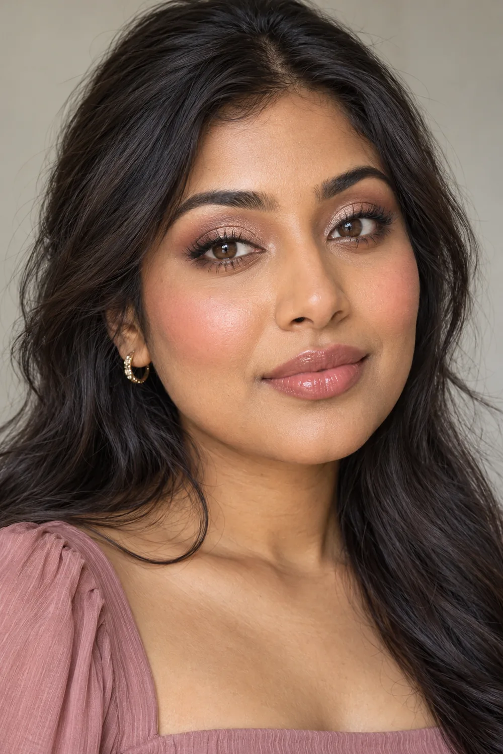 Adult South Asian woman with visible brown irises wearing rose-taupe crease shadow, champagne satin lids, smudged brown pencil liner, rosy blush, and glossy sheer rose lips.